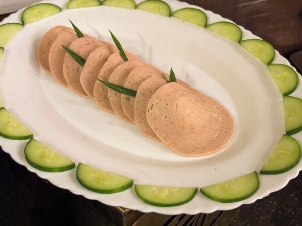 Un plato blanco con un alimento en capas, adornado con hojas verdes, rodeado de rodajas de pepino.