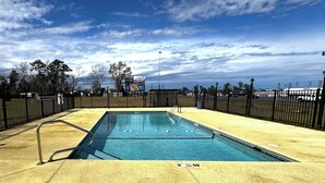 A rectangular swimming pool with a metal ladder and a fenced area, surrounded by a fence and trees. - Briarwood Motel Near Valdosta University I 75 (Valdosta)
