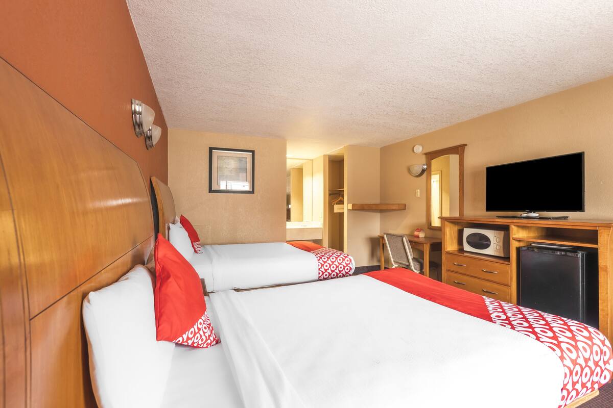 A hotel room with two beds, a television, a microwave, and a refrigerator.