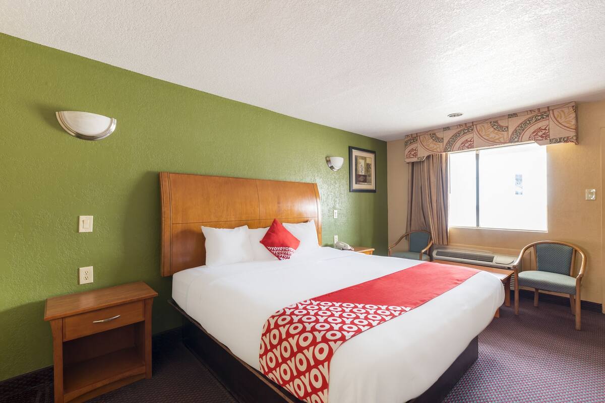 A hotel room with a large bed, a wooden headboard, a nightstand, a chair, and a window with curtains.