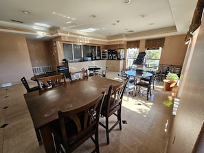 Un comedor amplio con una gran mesa de madera y sillas, una zona de cocina con mostrador y electrodomésticos, y vistas al exterior.