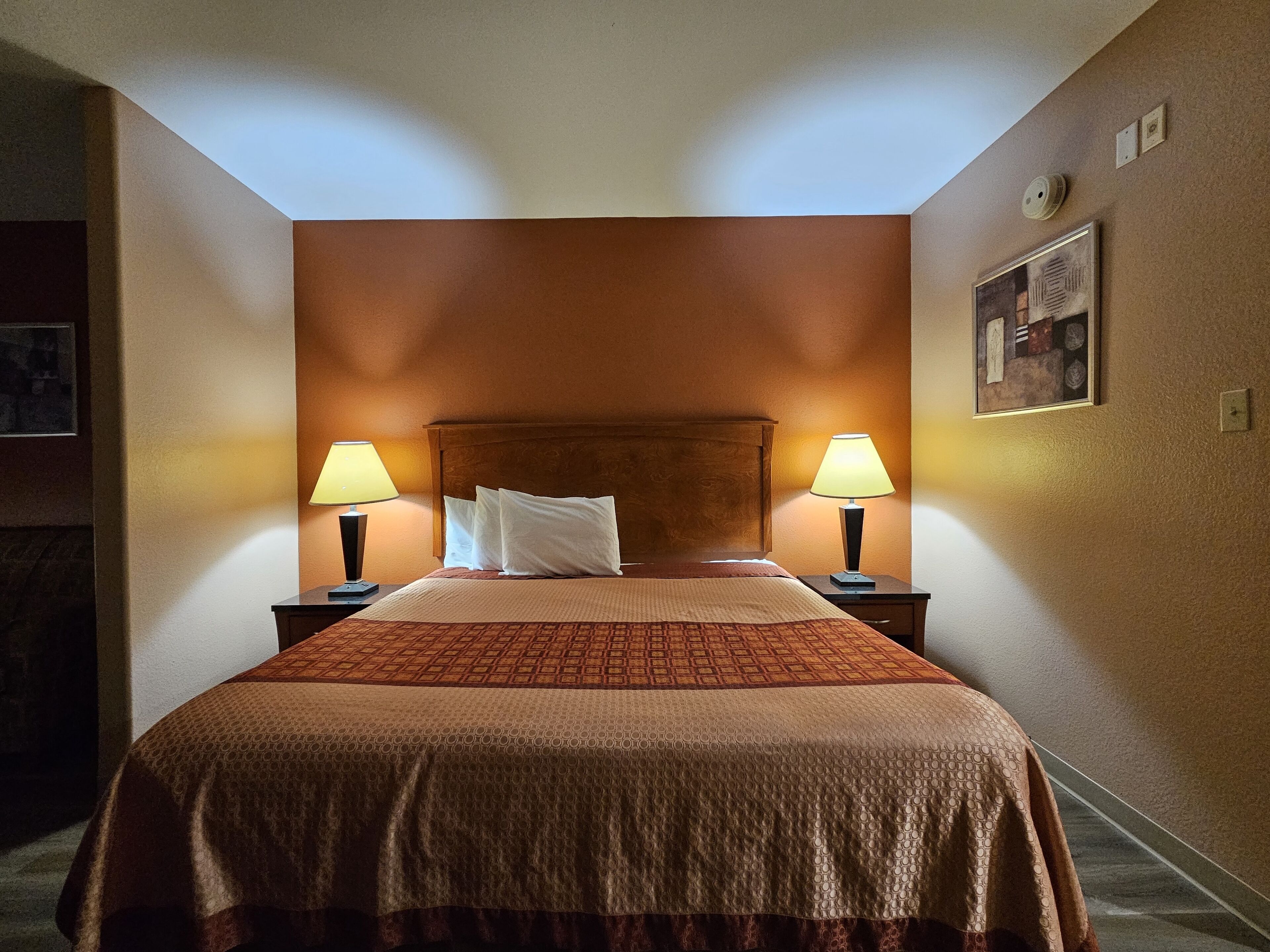 A hotel room with a large bed, two bedside lamps, a headboard, and a framed picture on the wall.