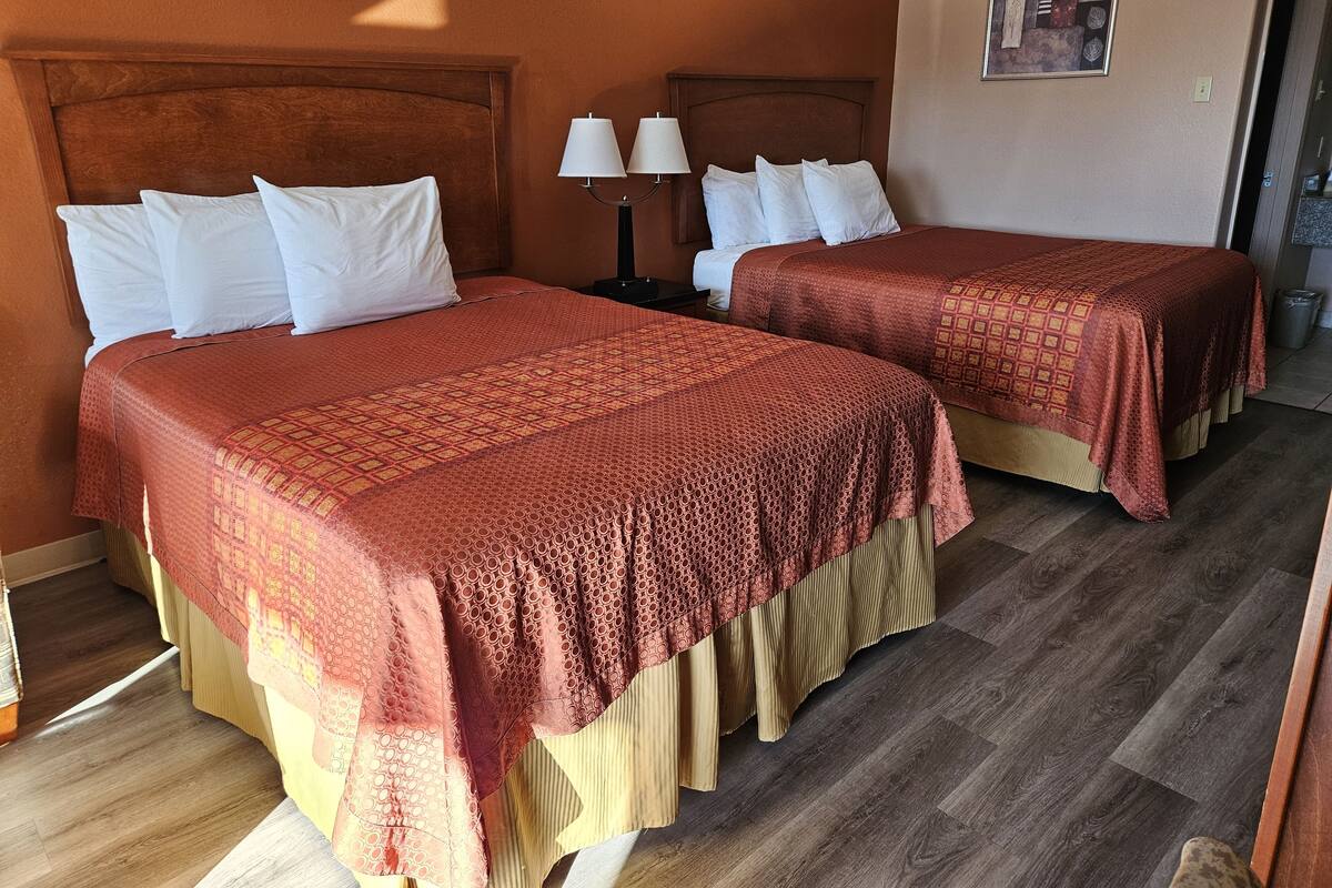 Quarto de hotel com duas camas, cada uma com almofadas brancas e colchas estampadas em vermelho. Um criado-mudo com abajur fica entre as camas.