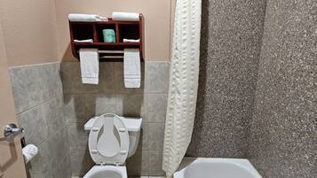 Une salle de bain avec des toilettes, une baignoire et un rideau de douche. Des serviettes sont suspendues sur une étagère au-dessus des toilettes.