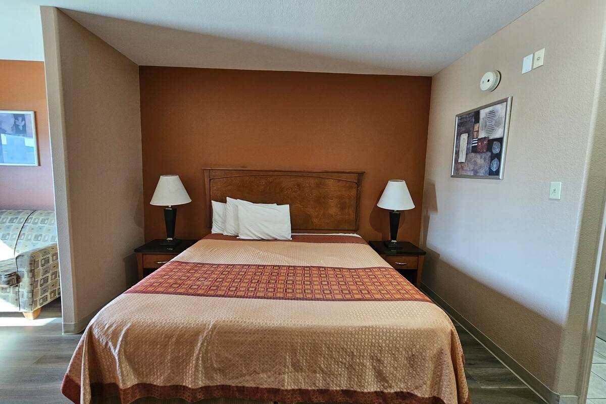 Quarto de hotel com uma cama grande, duas luminárias de cabeceira, uma cabeceira, um relógio de parede e um quadro emoldurado.