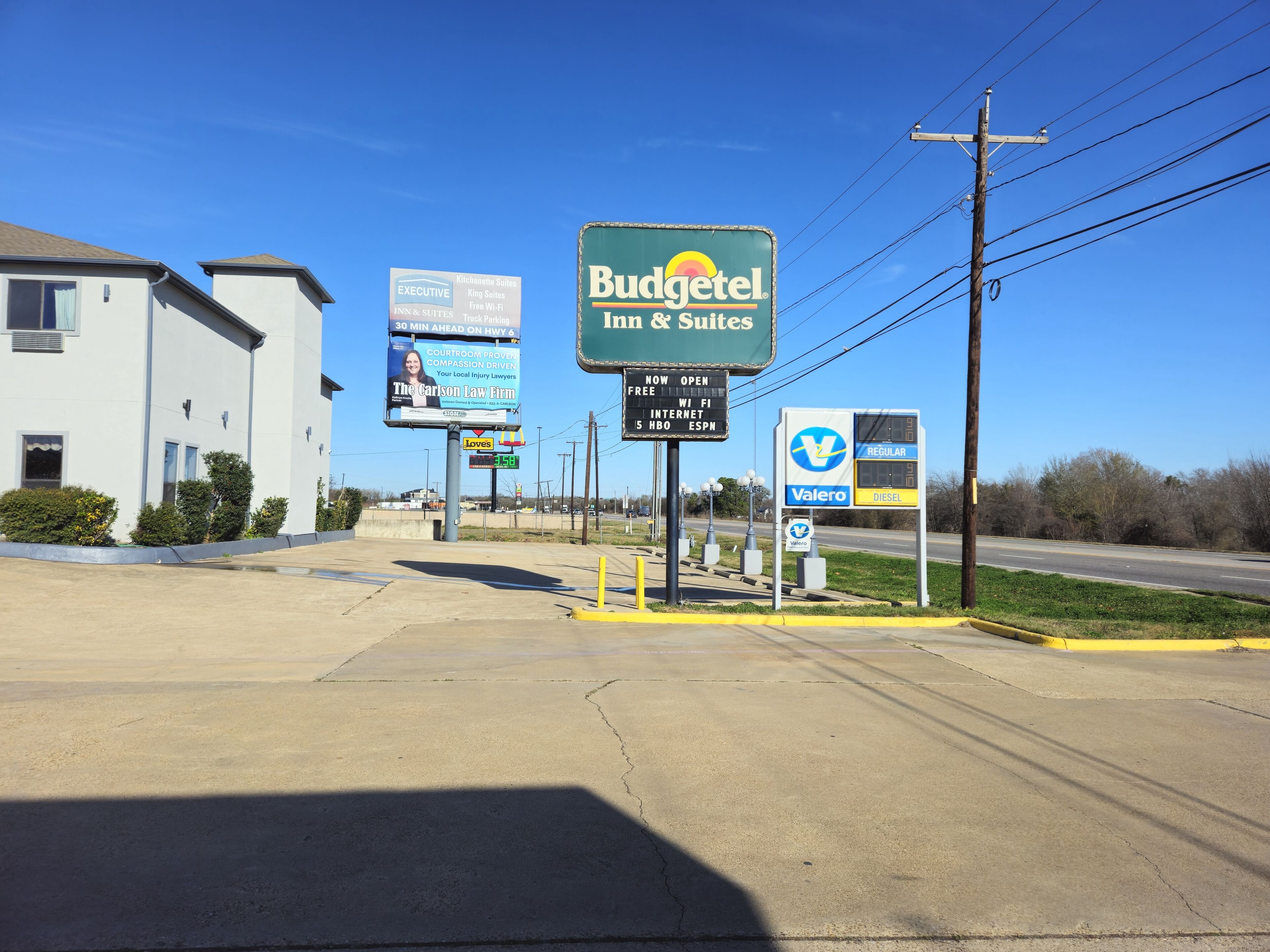 A Budgettel Inn & Suites sign, a Valero gas station, and a billboard for The Carlson Law Firm.