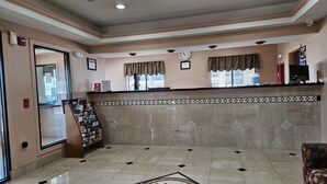 Zona de recepción con suelo de mármol, mostrador de recepción, un reloj y una ventana con cortinas.