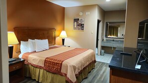 Habitación de hotel con una cama grande, dos lámparas de noche, televisión y baño visible a través de una puerta abierta.