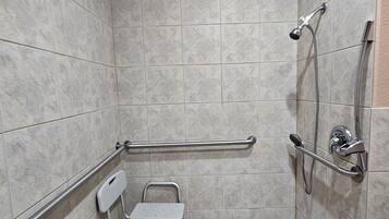 A small, tiled shower area with a grab bar, a wheelchair, and a handheld showerhead.