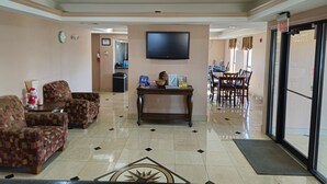 Un vestíbulo de hotel con sofás estampados, una mesa de centro, un televisor de pantalla plana y un comedor con sillas y mesas.