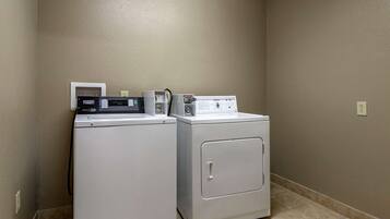 A laundry room with two washers and a dryer, a thermostat, and a power outlet on the wall.