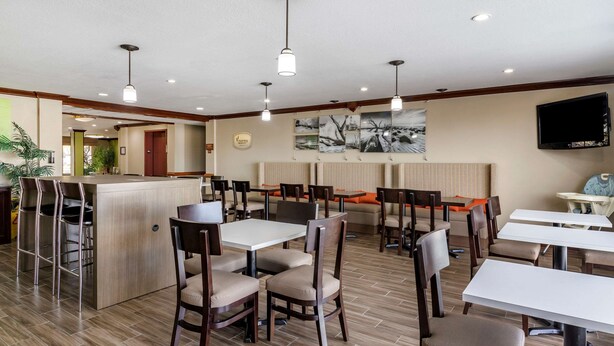 Um restaurante moderno com piso de madeira, mesas e cadeiras brancas e um espaço de bar.