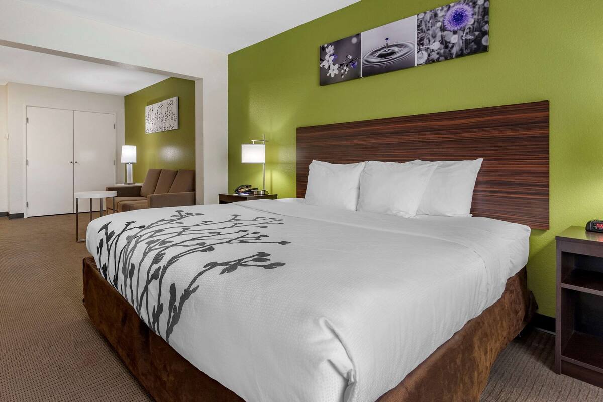 A hotel room with a large bed, a wooden headboard, two bedside tables with lamps, a chair, and a door.