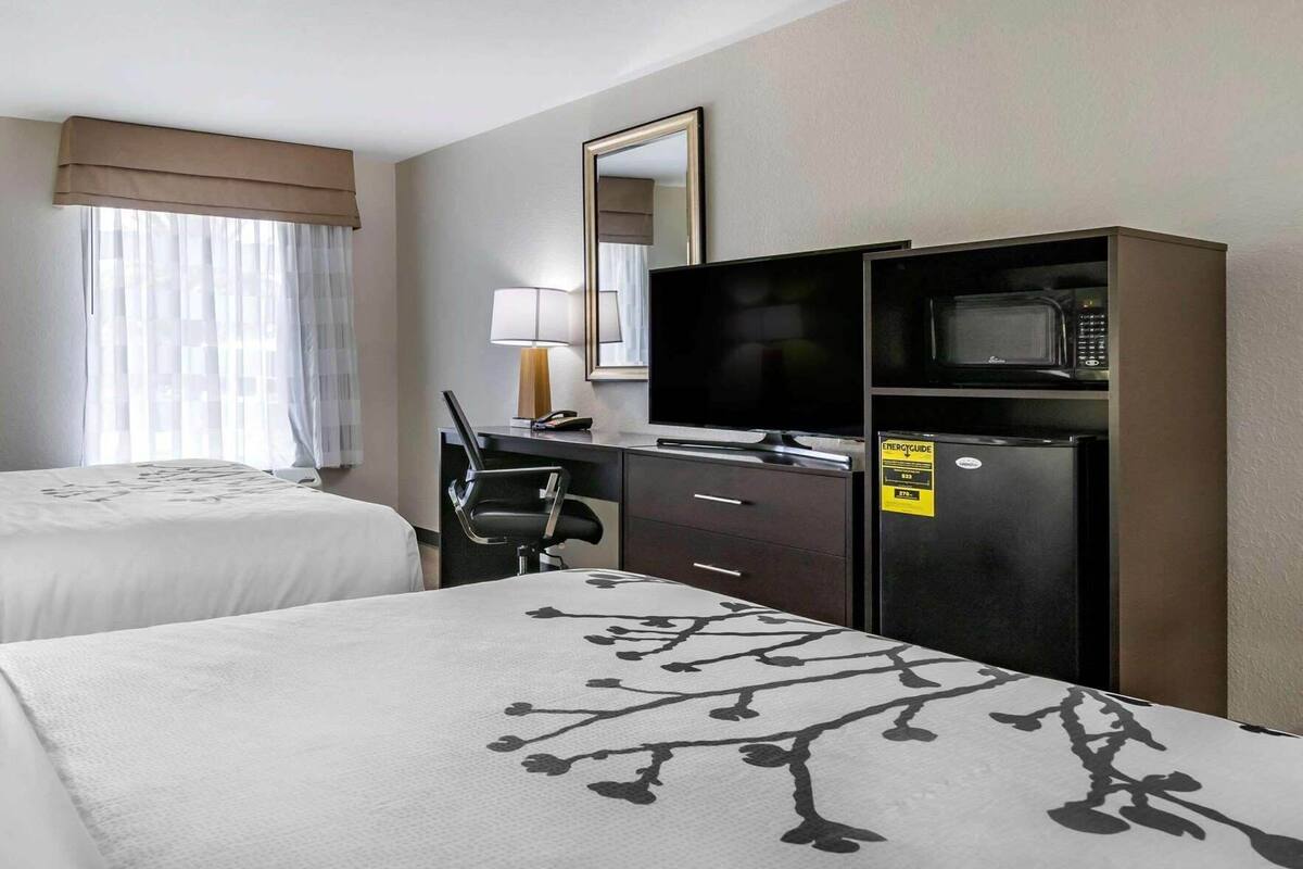 A hotel room with two beds, a desk with a computer, a television, and a refrigerator.