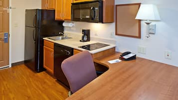 A compact kitchen with wooden cabinets, a stainless steel refrigerator, a microwave, a coffee maker, and a telephone on the table.