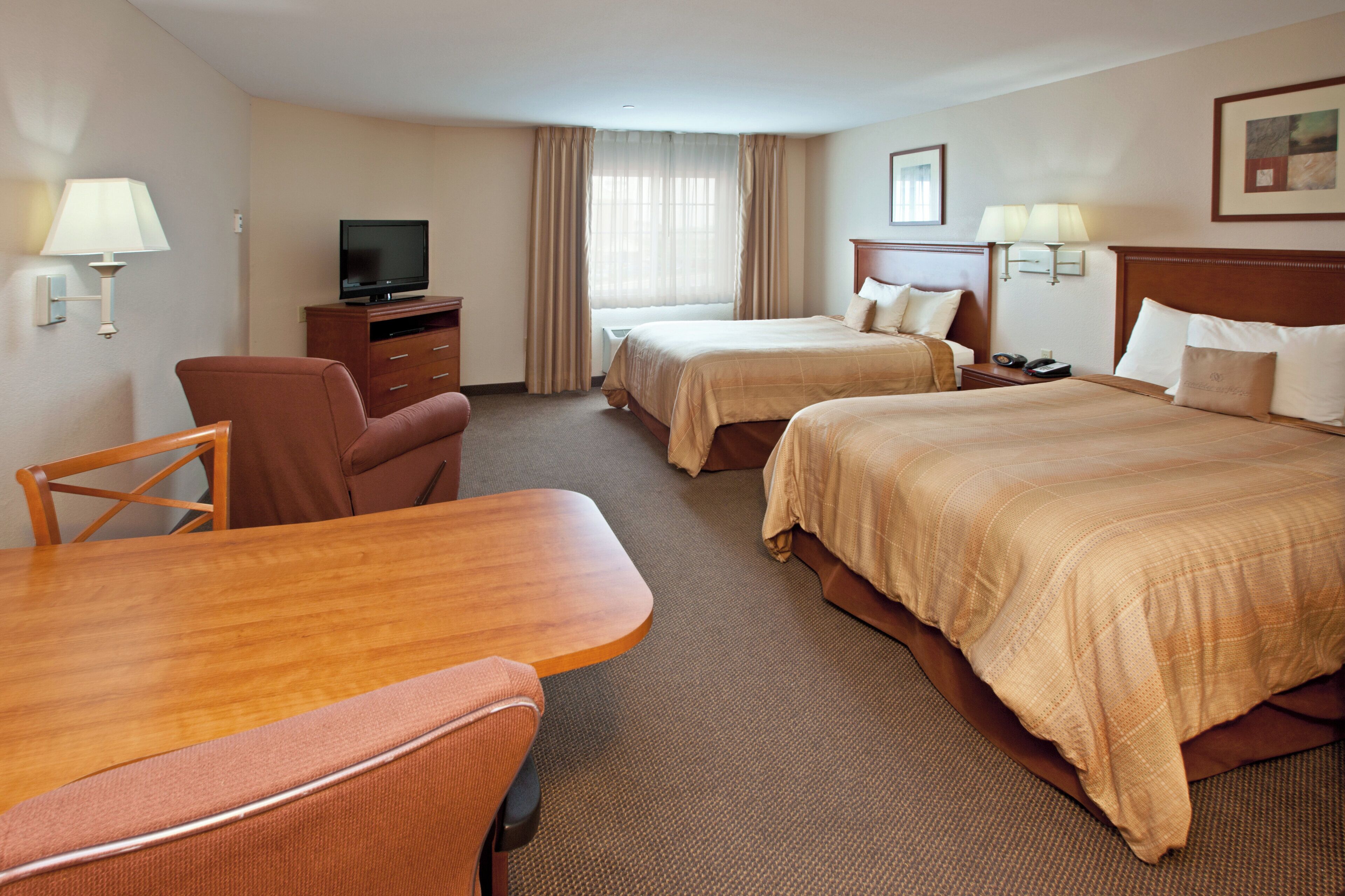A hotel room with a desk, two beds, a TV, and a window with curtains.