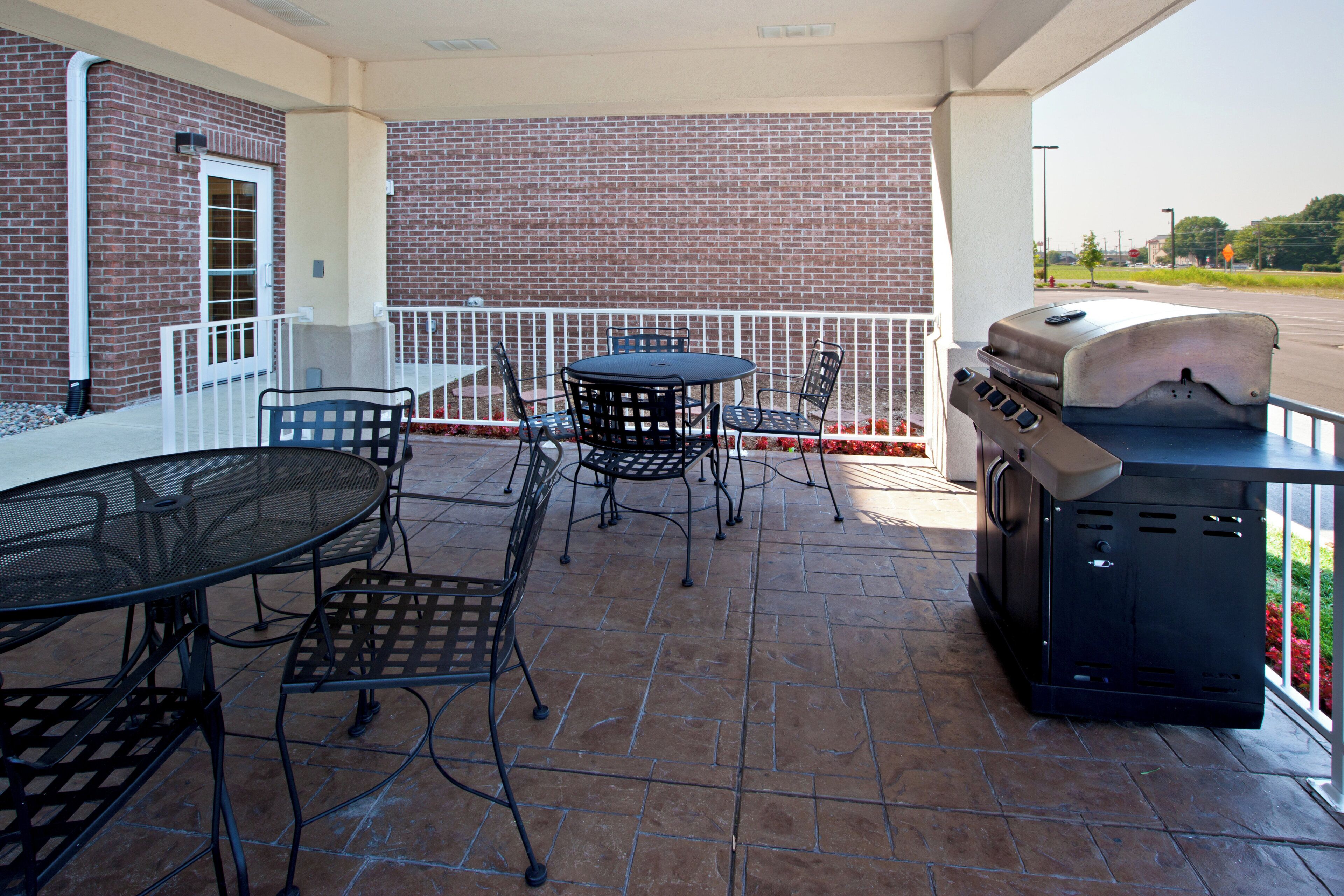 An outdoor patio with a brick wall, a round table, metal chairs, and a barbecue grill.
