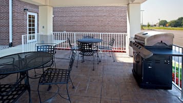 An outdoor patio with a brick wall, a round table, metal chairs, and a barbecue grill.