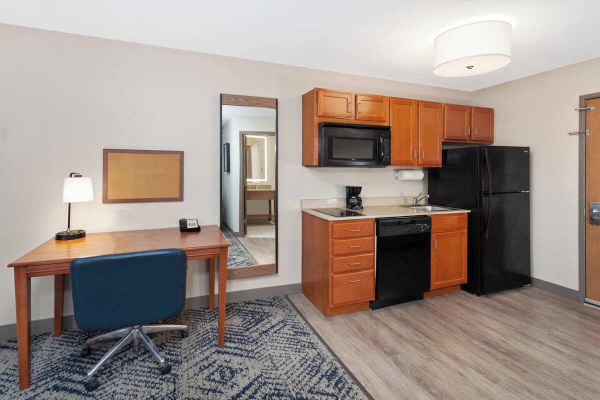 A compact kitchen with wooden cabinets, a black refrigerator, a microwave, and a coffee maker.