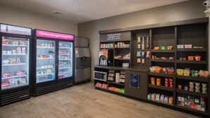 A section of a store with refrigerated beverage dispensers, shelves stocked with snacks, and a coffee machine. - Candlewood Suites Louisville North by IHG (Clarksville)