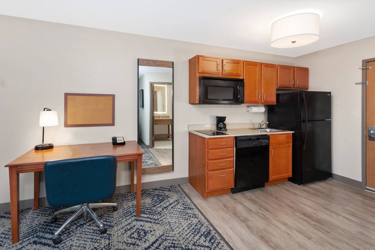 A compact kitchen with wooden cabinets, a black refrigerator, a microwave, and a coffee maker.