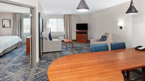 A hotel room with a bed, a sofa, a dining table, a TV, and a desk. - Candlewood Suites Louisville North by IHG (Clarksville)