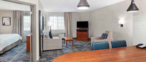 A hotel room with a bed, a sofa, a dining table, a TV, and a desk.