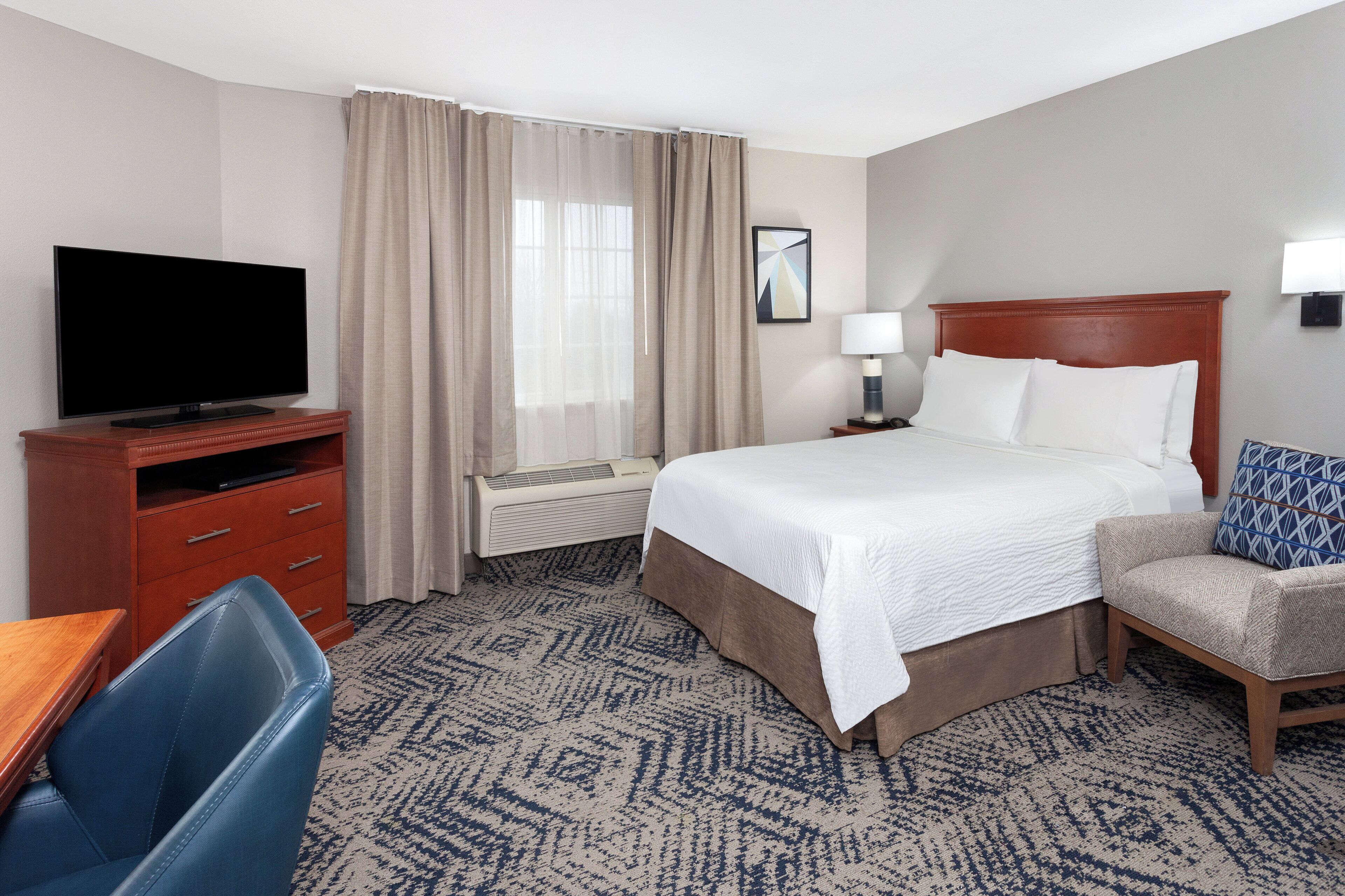A hotel room with a bed, a TV, a desk, and a chair.
