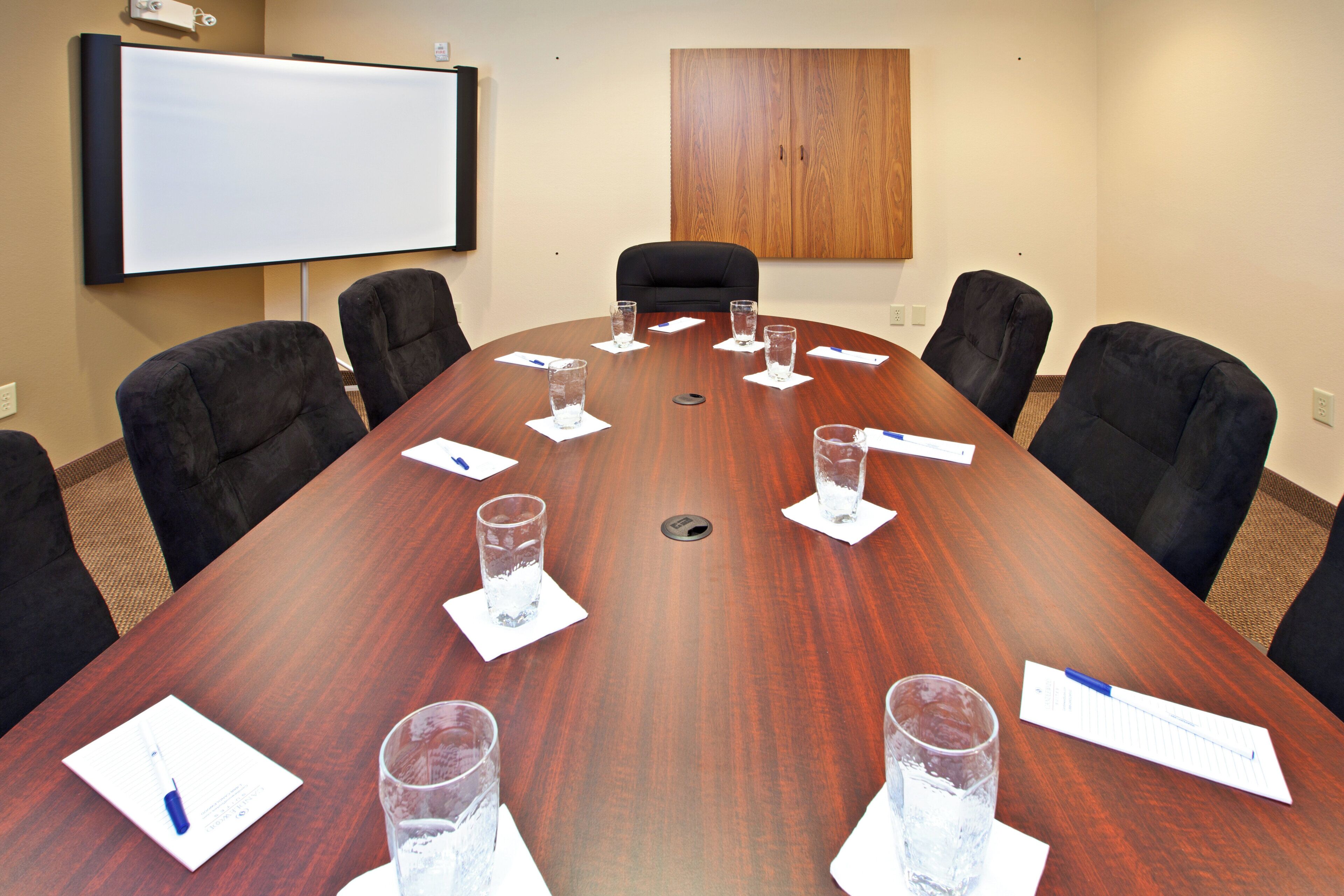 Une salle de conférence avec une grande table en bois, six chaises, un tableau blanc et un meuble en bois.