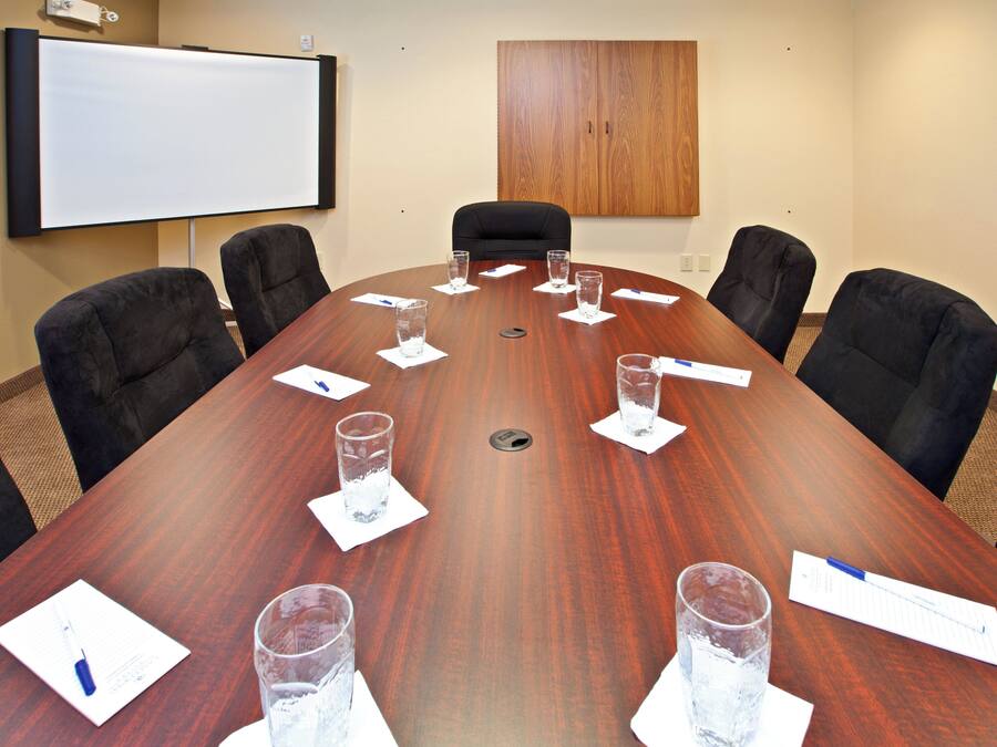 Une salle de conférence avec une grande table en bois, six chaises, un tableau blanc et un meuble en bois.