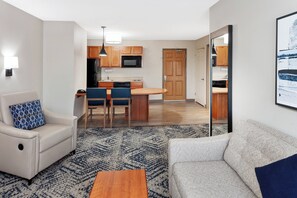 A compact living space with a sofa, a chair, a small table, and a kitchen area with a microwave and cabinets. - Candlewood Suites Louisville North by IHG (Clarksville)
