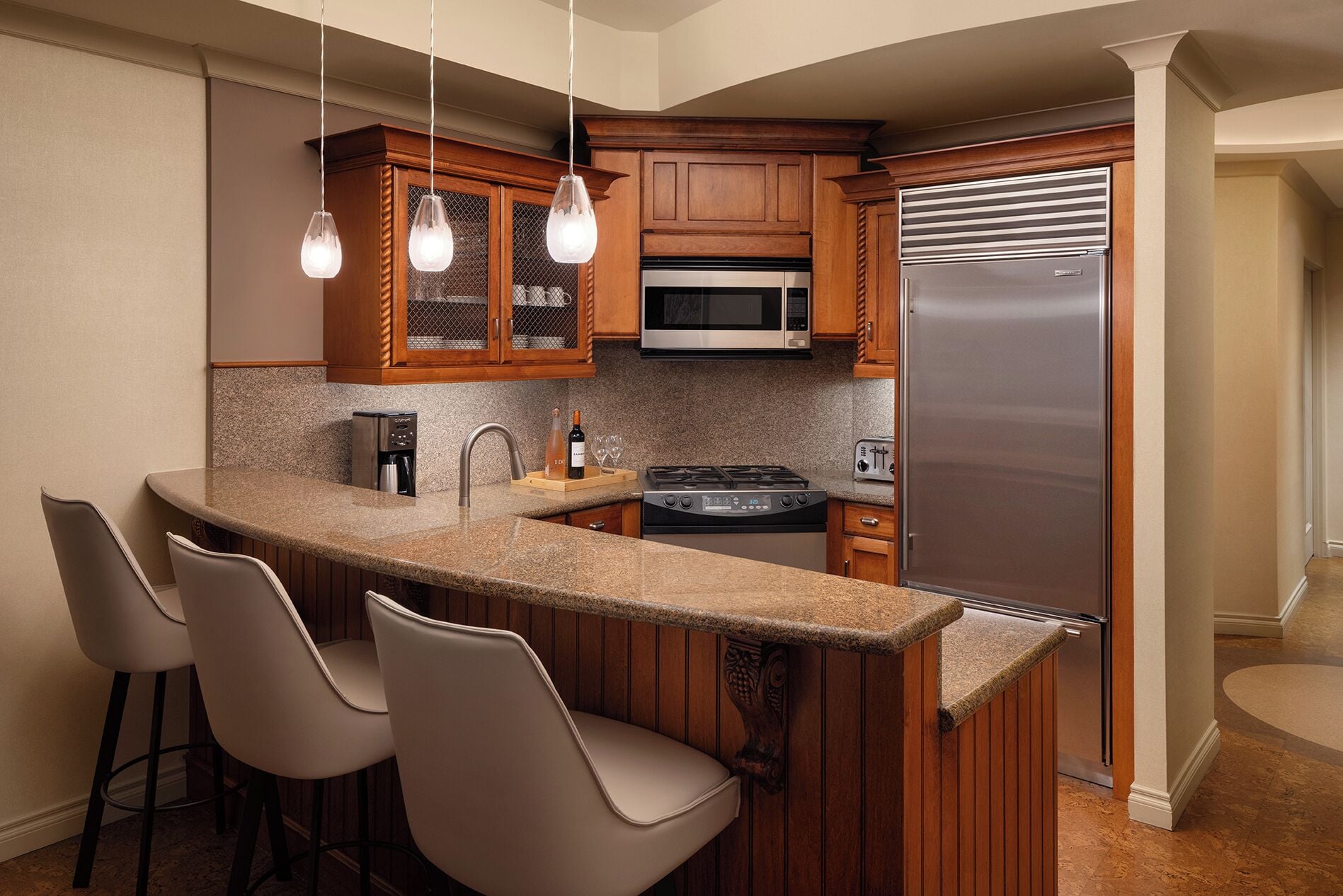 A kitchen with a granite countertop, stainless steel appliances, wooden cabinets, and pendant lighting.