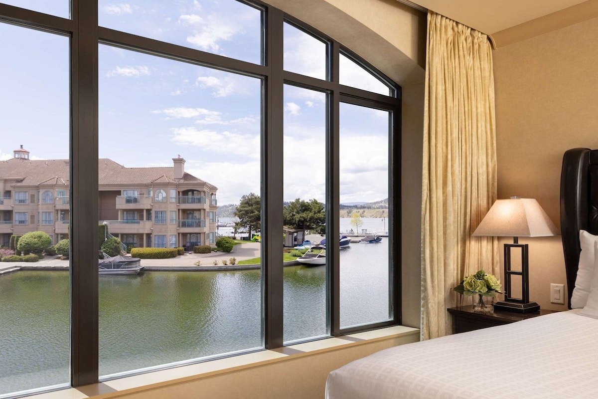 A hotel room with a large window offering a view of a building and a body of water.