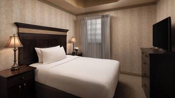 A hotel room with a large bed, two bedside tables with lamps, a TV, and a window with curtains.