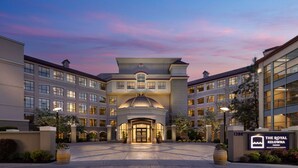A hotel entrance with a central archway, multiple floors, and a sign for The Royal Kelowna.