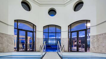 Une piscine avec vue sur le ciel nocturne, grâce à de grandes fenêtres, entourée de murs et d’un sol recouverts de carreaux.