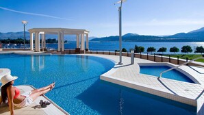 A swimming pool with a view of a lake and mountains, a gazebo, and a lamp post.