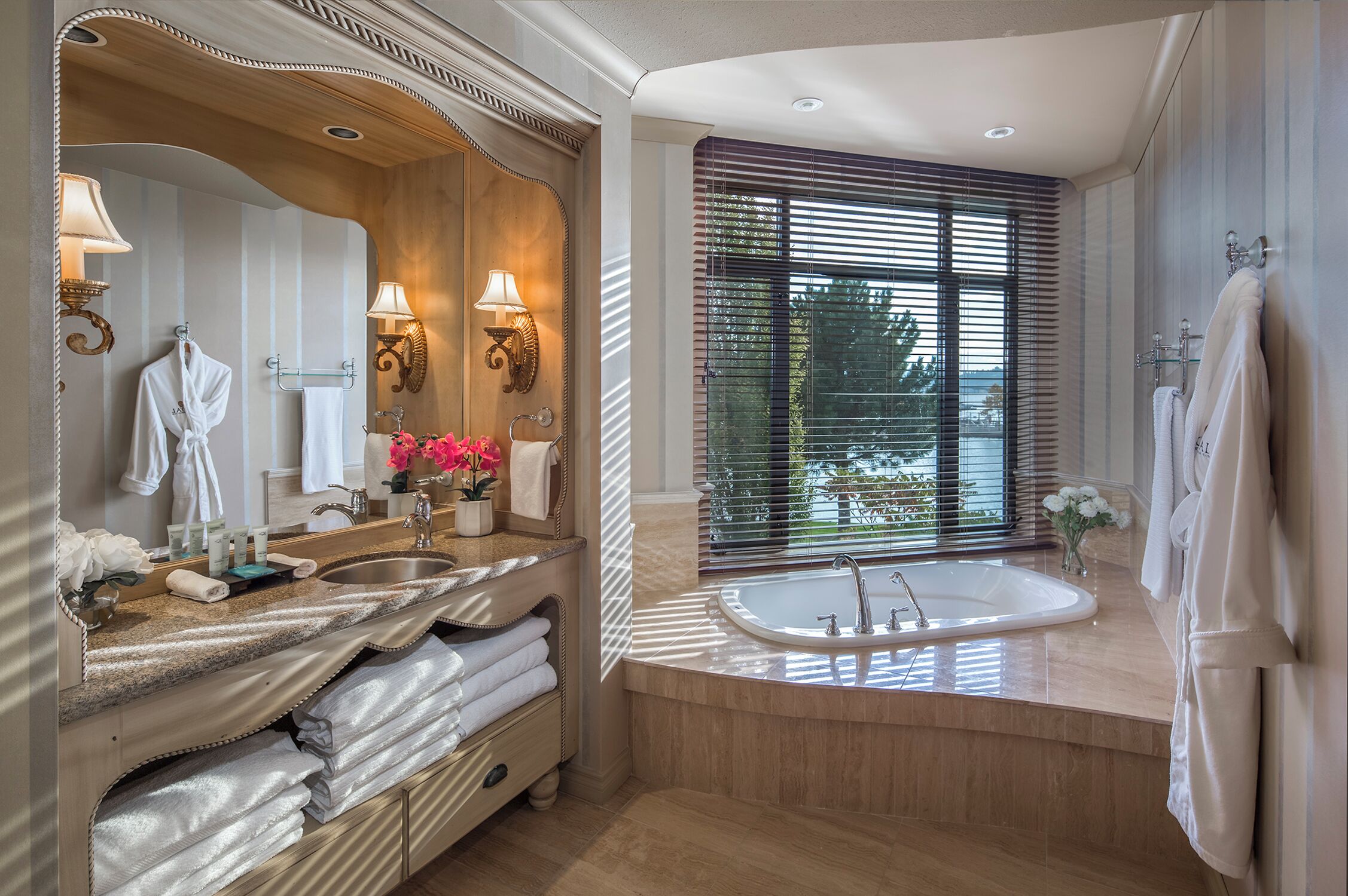 A modern bathroom with a large mirror, vanity, bathtub, and a window with blinds.