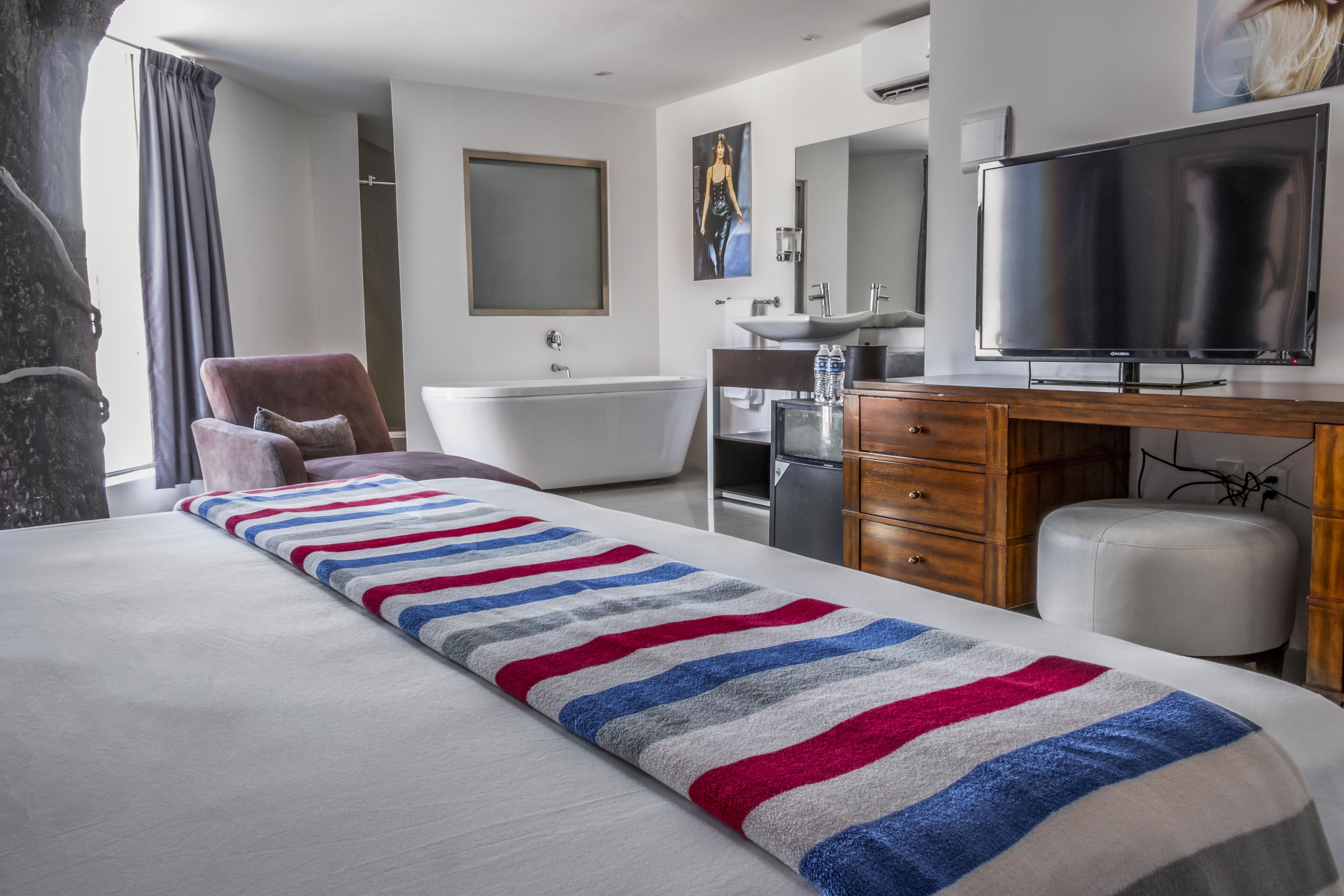Quarto de hotel moderno com uma cama grande, uma escrivaninha de madeira, televisão de tela plana, banheira e uma janela ampla com cortinas.