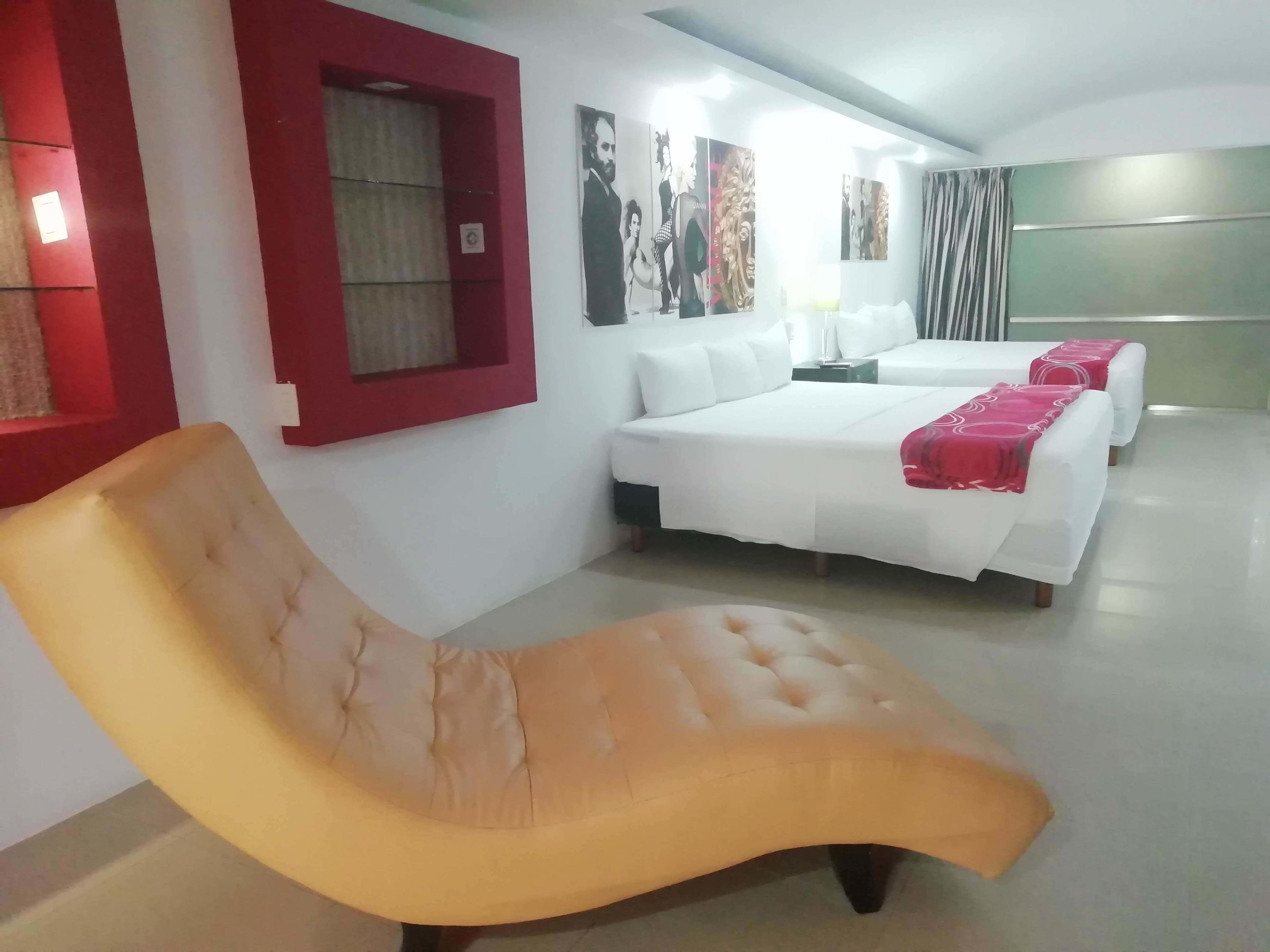 A hotel room with a large bed, a sofa, and a window with red trim.