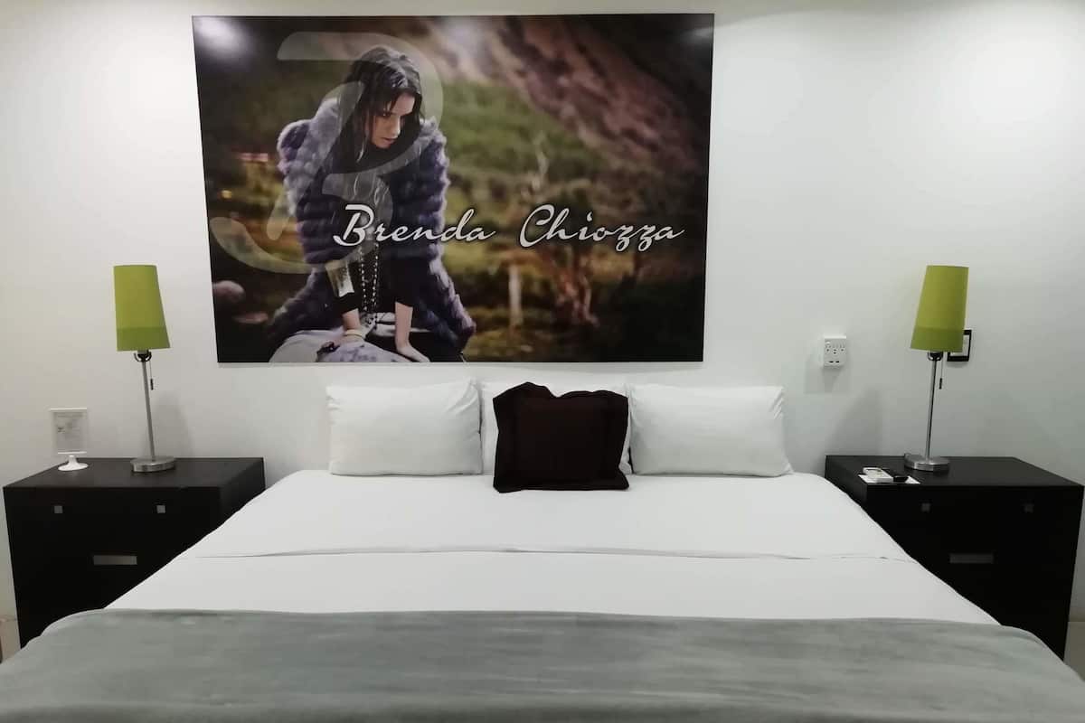 A hotel room with a large bed, two bedside tables with lamps, a wall-mounted artwork, and a white bedspread.