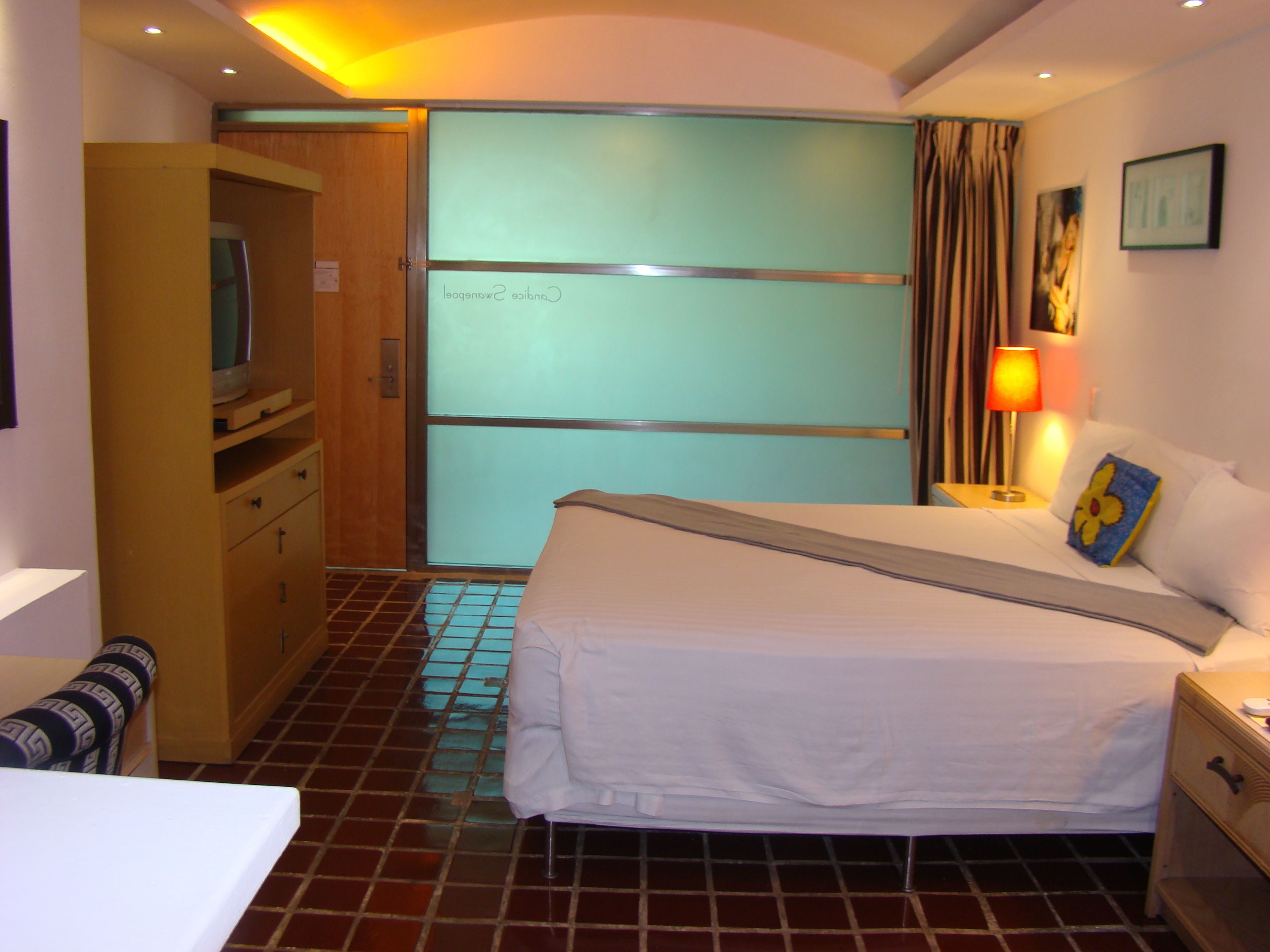 A hotel room with a bed, a desk, a chair, a wardrobe, and a television.