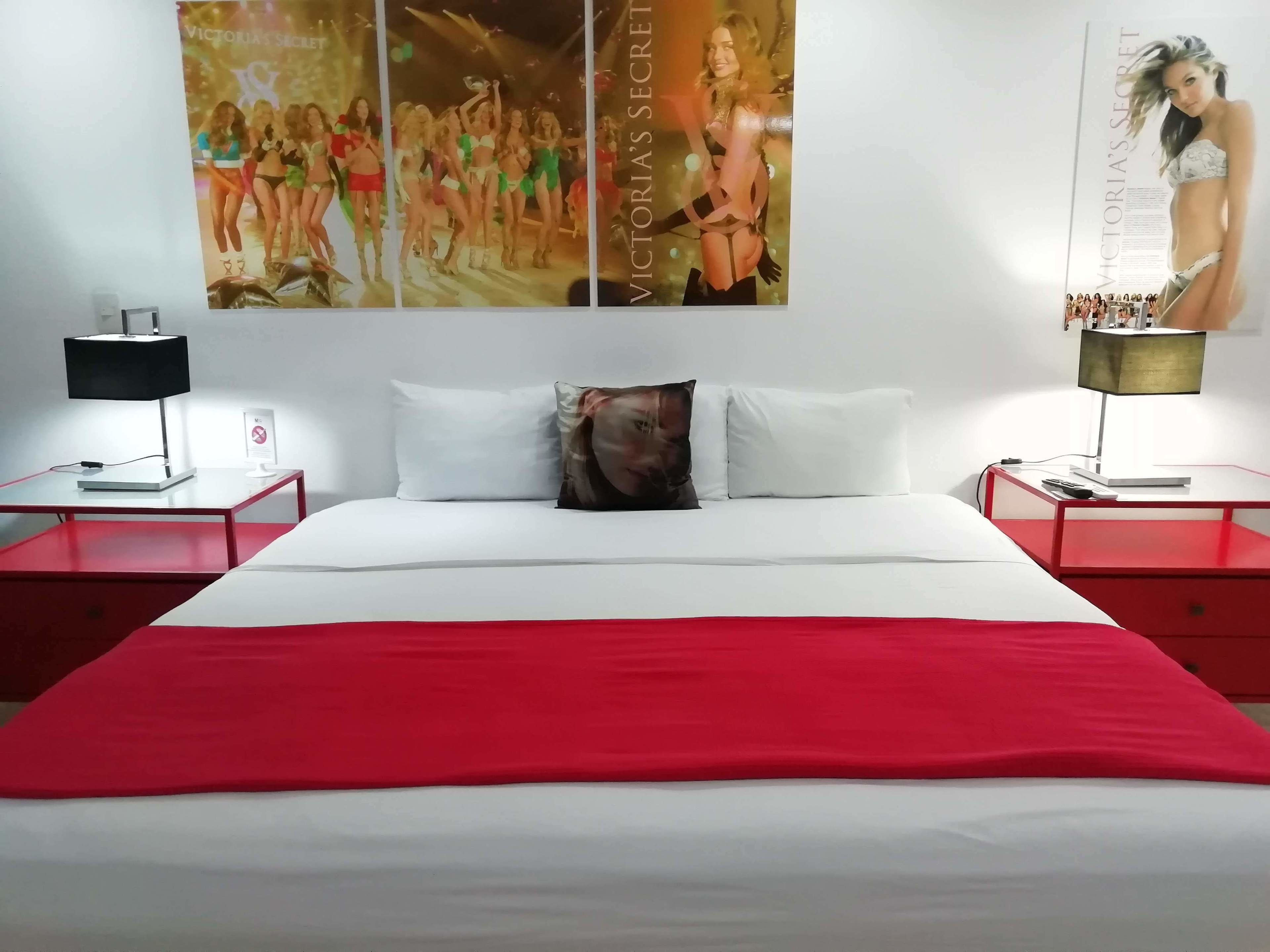 A bed with a red and white bedspread, two bedside tables with lamps, a pillow, and two posters on the wall.