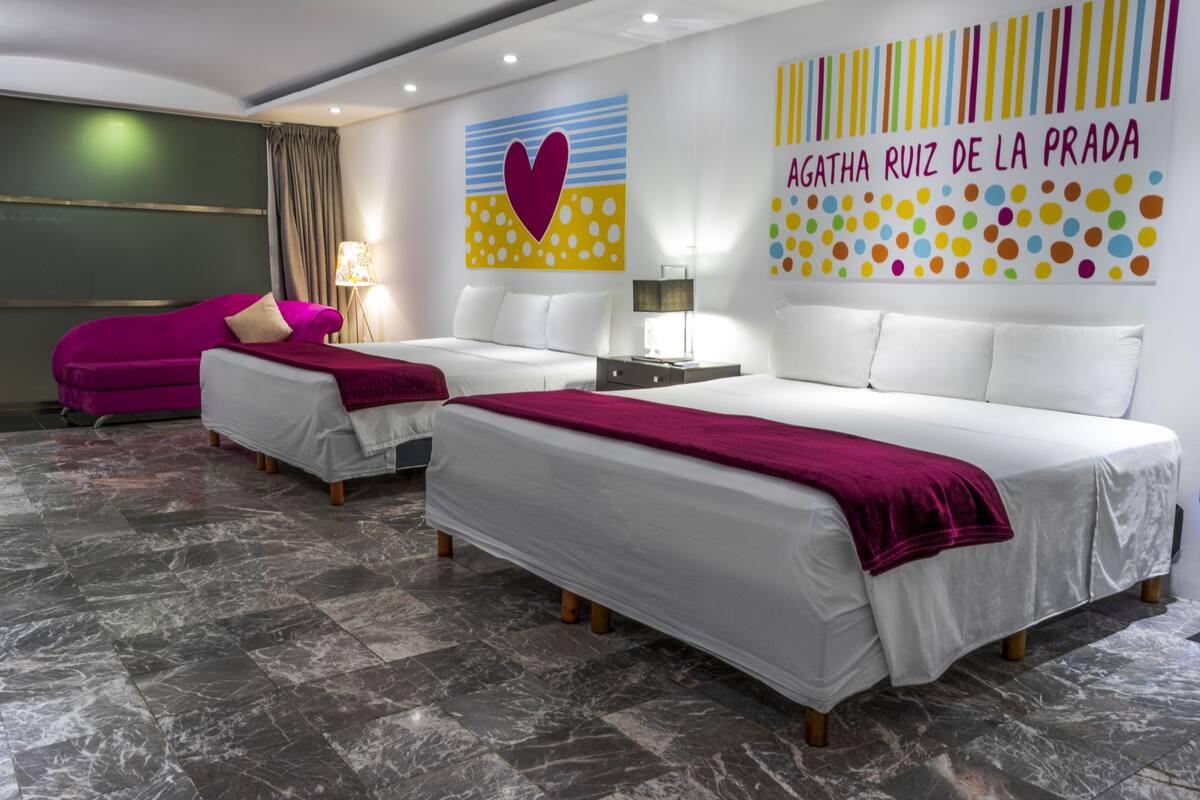 A hotel room with two beds, a purple sofa, and a large wall art piece.