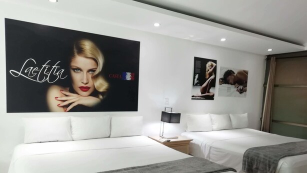 Une chambre d’hôtel avec deux lits, une table de chevet avec une lampe et une grande affiche au mur.