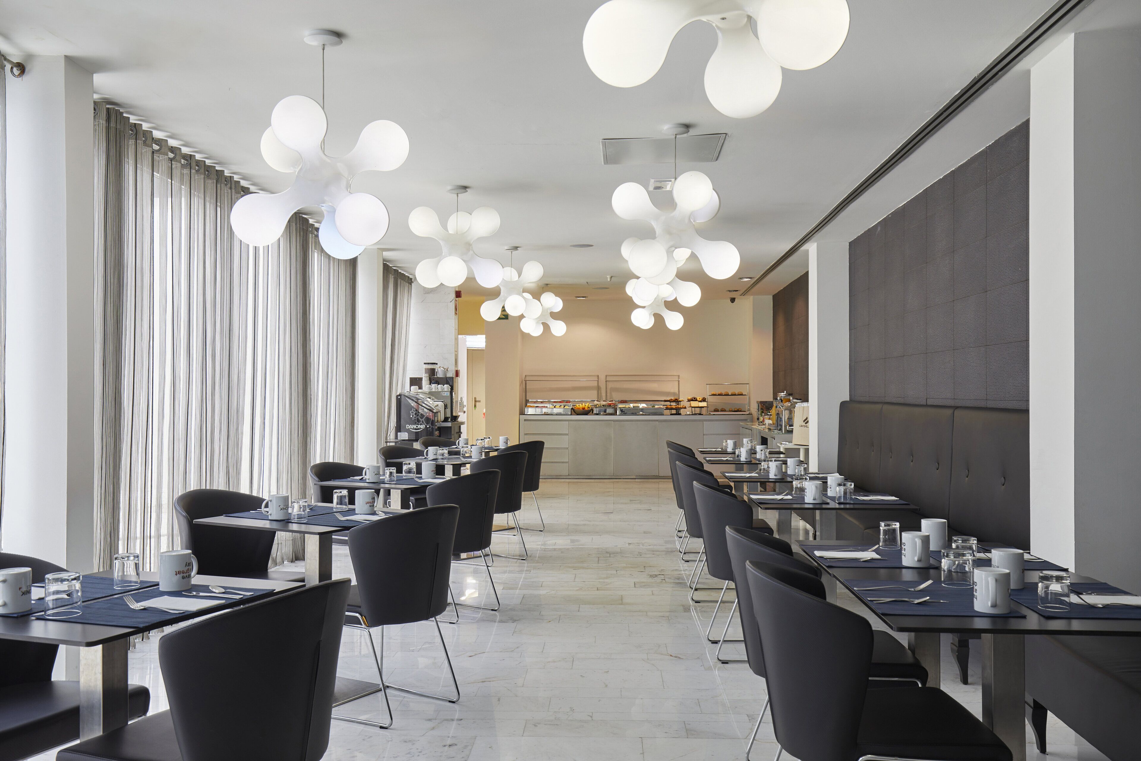 A modern hotel dining area with long tables, black chairs, and unique spherical ceiling lights.