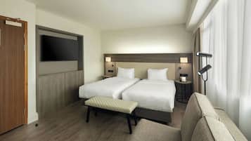 A hotel room with two beds, a TV, bedside lamps, a bench, and a sofa.
