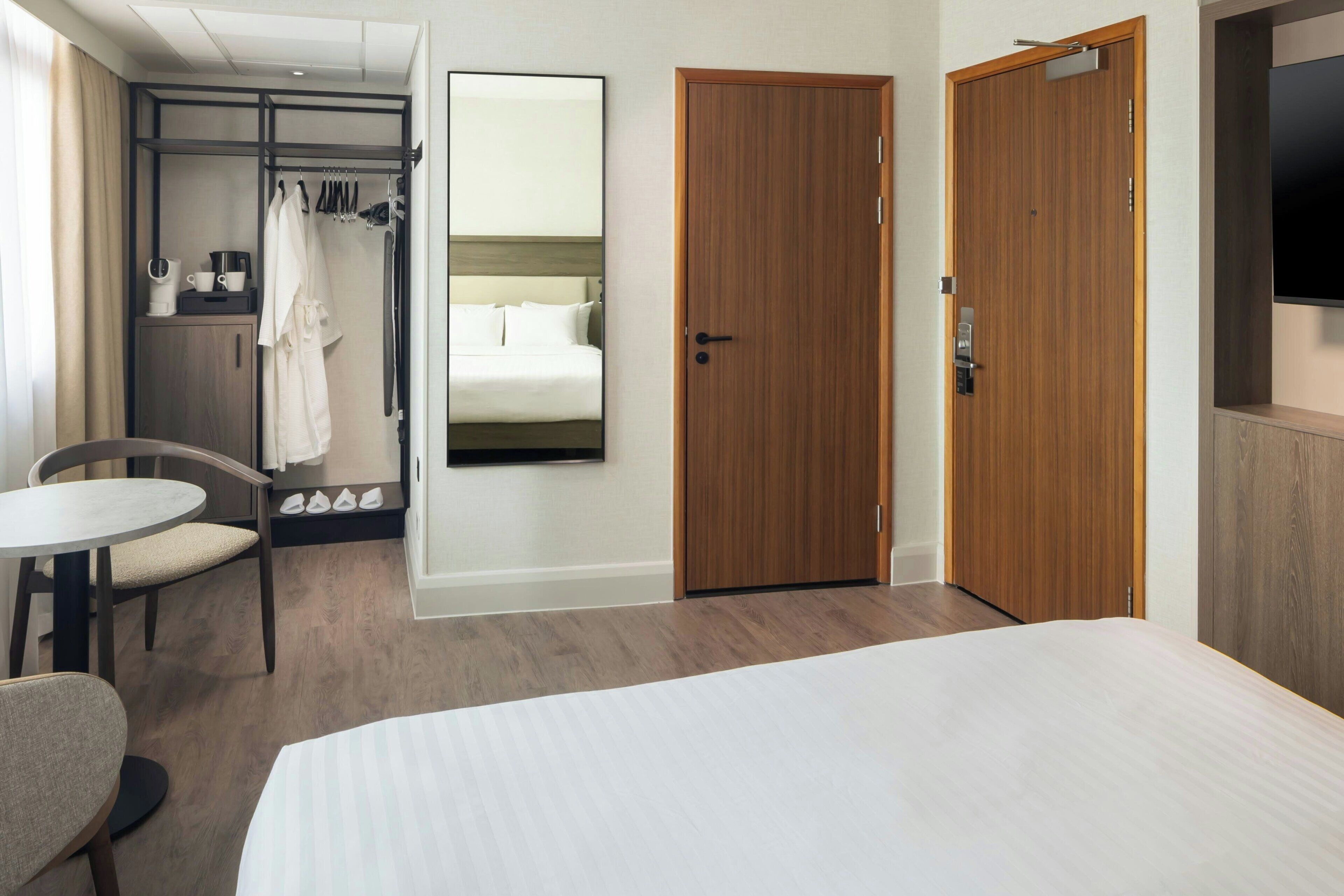 A hotel room with a bed, a desk, a chair, a wardrobe, a mirror, and a television.