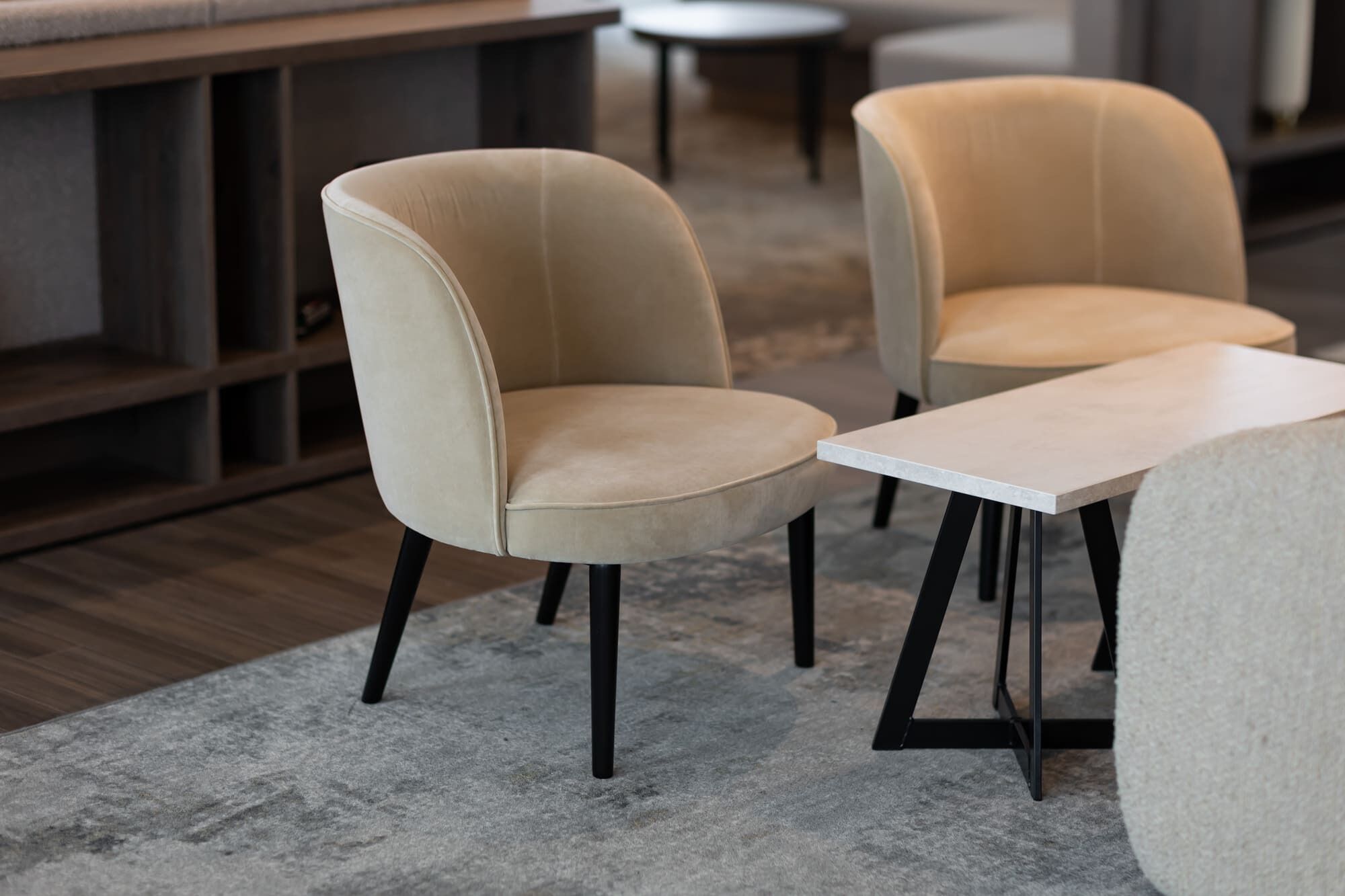Two armchairs with black legs, a small round table, and a grey carpeted floor.