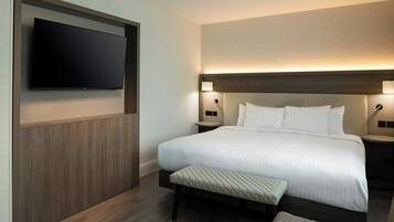 Quarto de hotel com uma cama grande, televisão de tela plana na parede, abajures e detalhes em painéis de madeira.